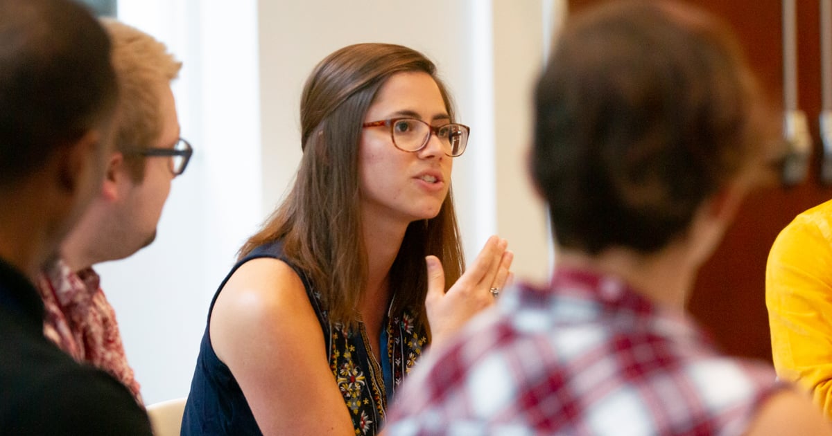 A woman in brown rimmed glasses speaking to other students while gesturing with her hands