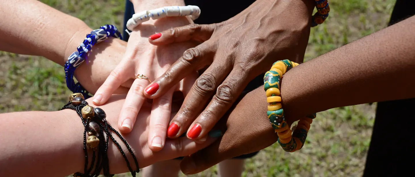 People putting their hands together in a huddle. Each person is wearing a chunky bead bracelet.